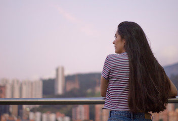 Fototapeta na wymiar Chica mirando a un lado de la ciudad. Edificios y montañas al fondo. Medellin Colombia