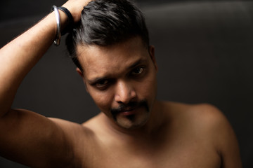 Fototapeta na wymiar Face portrait of a confident muscular Indian brunette dark skinned macho man in bare body and underwear brief standing in black background. Indian lifestyle and fashion portrait