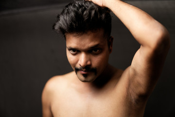 Fototapeta premium Face portrait of a confident muscular Indian brunette dark skinned macho man in bare body and underwear brief standing in black background. Indian lifestyle and fashion portrait