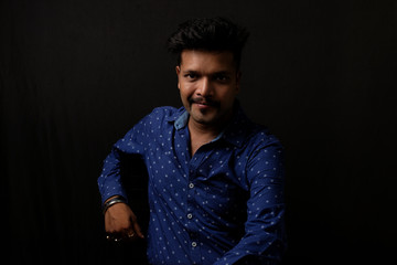 Portrait of a handsome and intelligent Indian brunette man wearing blue shirt with white stars sitting on a chair. Indian lifestyle and fashion portrait