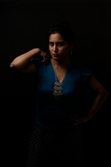 portrait of a beautiful Indian Bengali brunette woman in light and shadow before a black copy space background wearing a blue top. Indian lifestyle and fashion  portrait