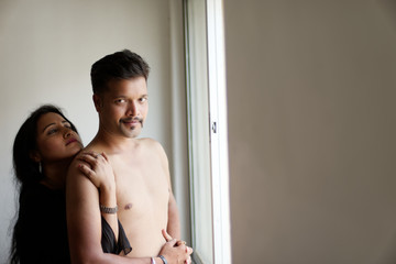 Indian Bengali beautiful brunette couple sharing intimate romantic moments standing in front of a window in white background. Indian lifestyle  and romantic couple