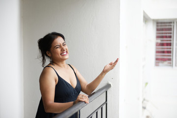 Portrait of a beautiful Indian Bengali brunette woman wearing a black western dress enjoying rain while standing on her balcony. Indian lifestyle and fashion portrait