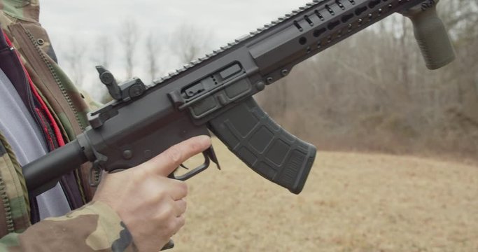 Man loads a magazine into an automatic rifle and chambers a round