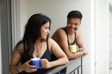 Indian Bengali beautiful brunette couple in black dress sharing intimate romantic moments while drinking tea/coffee standing on balcony in white background. Indian lifestyle  and romantic couple