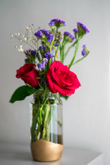 Fototapeta na wymiar Red roses with purple flowers bouquet in a clear glass jar. Repurpose, from trash to treasure idea.