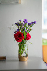 Red roses with purple flowers bouquet in a clear glass jar. Repurpose, from trash to treasure idea.