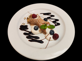 Sicilian and Italian Cannoli dessert on white plate with raspberries and blueberries, isolated on black background