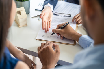 Young Asian couple making contract with house sale agency. Man signing the contract and his wife...