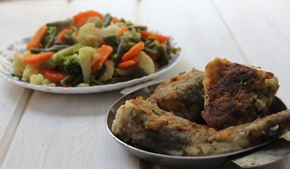 fish fried in flour and stewed vegetables on a white wooden background