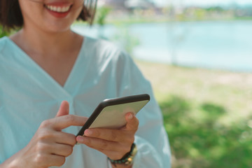 Woman happy and smile while use smartphone to do work business, social network, communication in public nature area.