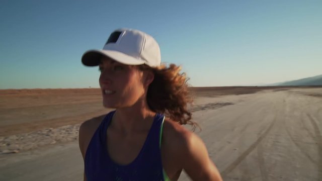 Portrait of caucasian girl jogging in dry desert at sunrise rapid slow motion