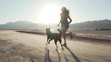 Fit female runs with her funny dog in dry desert at sunrise