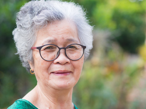 Close-up of face elderly woman smiling happiness, short white hair and looking at the camera, standing in garden. Asian senior woman healthy and have positive thoughts on life make her happy every day
