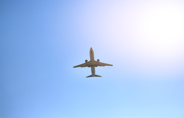 Airplane flying on blue sky background with rays of sunlight. Below view