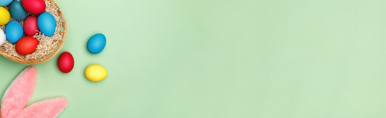 Easter basket with colored eggs and rabbit ears on a background of green mint. Copy space banner top view flat lay
