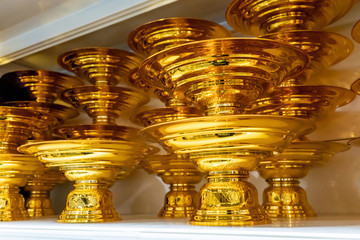 Stack of Thai traditional golden tray on white shelve.