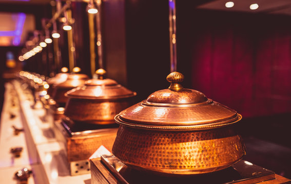 Close Up Of Traditional Rajasthani Food Buffet Served In Copper Chafing Dish In A Luxury Indian Hotel Restaurant At A Wedding Ceremony. Antique Style Utensils Placed In A Row At A Marriage Hall.