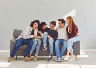 A group of friends is sitting on couch in a room on a gray background.