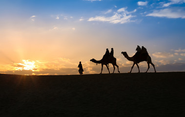 Tourist on camel back in silhouette at sunset at Thar deser Jaisalmer Rajasthan, India