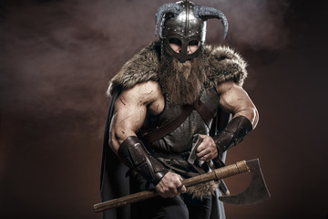 Medieval warrior berserk Viking with axes attacks enemy. Concept historical photo of Scandinavian god in armor and helmet with horns