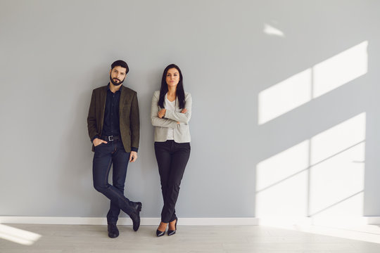A businessman and a business woman are standing against a gray wall