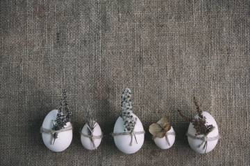 Zero waste, vegan, sustainable Easter mockup. Row of wooden eggs decorated with dried flowers on natural canvas burlap background. Feeling nature, moody floral, eco-friendly postcard.
