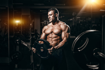 Plakat Muscular man bodybuilder training in gym and posing. Fit muscle guy workout with weights and barbell