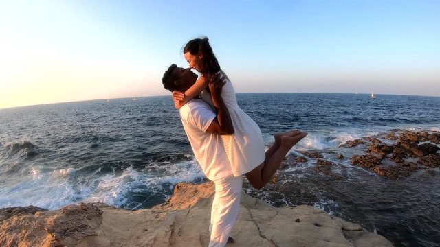 Young, in love and interracial couple kissing by the shore in Malta, slow motion