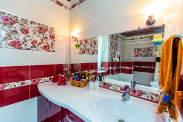 Large bathroom in the cottage in red and white colors. Maroon and white tiles, tiles with red colors. Toilet, shower. White and maroon tiles on the floor