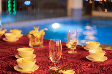 Empty glasses on table prepared for dinner next to swimming pool at night.