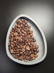 in a ceramic bowl, roasted coffee beans on a black background.