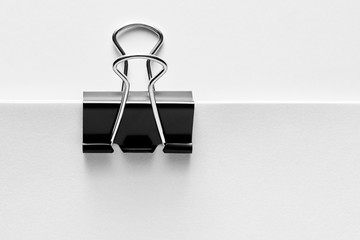 Black binder clip attached to the corner of a blank white paper