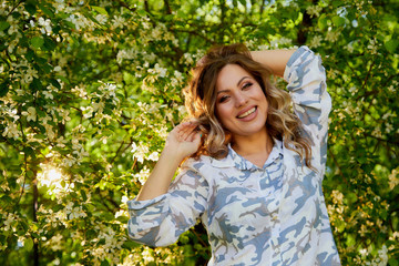 Portrait of a beautiful blonde girl with green eyes and blossoming apple tree with white flower in the park in a spring time