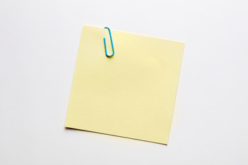 Blank yellow note paper or notepad with a blue paper clip on white background with copy space