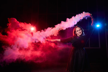 Teenage chubby girl with colored smoke torch in hand during photoshoot with colored smoke at night...