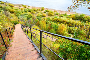 Top view of a large wooden staircase leading to the water of a river or lake and green trees, bushes and plants near it in a Park on the shore