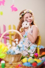 child-a little girl in a dress and a flower wreath on her head smiling and holding an Easter Bunny on the background of flowers and decor