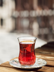 Tea in a glass of armudu on a saucer, located on a wooden table in the loggia. Bright sunny day. Close-up.
