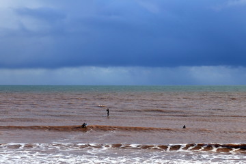Fototapeta na wymiar Surfers in wetsuit enjoying surfing on a cold rainy winter day in Sidmouth, Devon