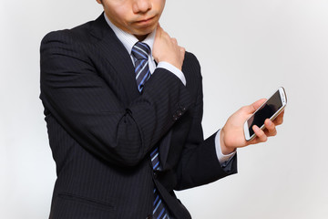 肩こりに悩むスーツ姿の男性　血行不良　スマートフォン