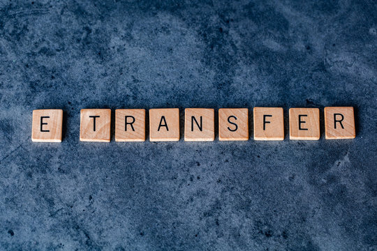 "E-Transfer" (Electric Transfer) spelled out in wooden letter tiles on a dark rough background