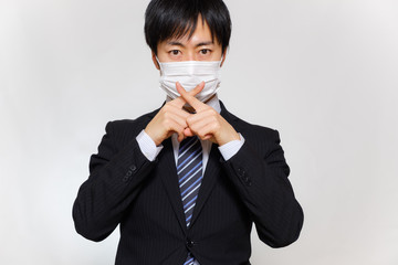 マスクをしてNGサインを出すスーツ姿の男性