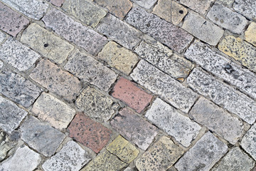 A fragment of an old cobblestone pavement lined with multi-colored rectangular bricks. Close-up. Background. Pattern.