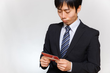 預金通帳を見て悩むスーツ姿の男性　浪費　借金　貧乏　不況　