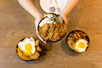 Hand holding bowl of rice with stir fried pork in Japanese style.