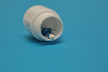 Capsules / tablets in open white pharmaceutical bottle on aquamarine background
