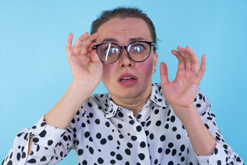 Portrait of a frightened woman with glasses on a blue background in the studio. The emotions of fear. Hand holds glasses.