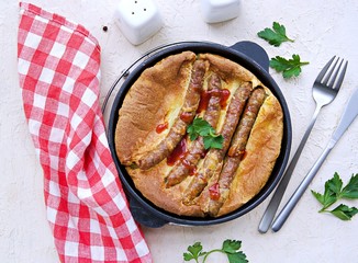 Pork sausages baked in pastry for Yorkshire pudding in a serving cast-iron skillet on a light concrete background. Toad in a hole recipe. British cuisine. Top view.