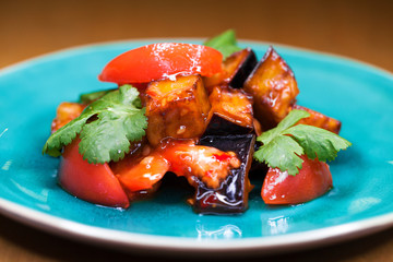 Salad of tomatoes and fried eggplant with sauce on blue plate